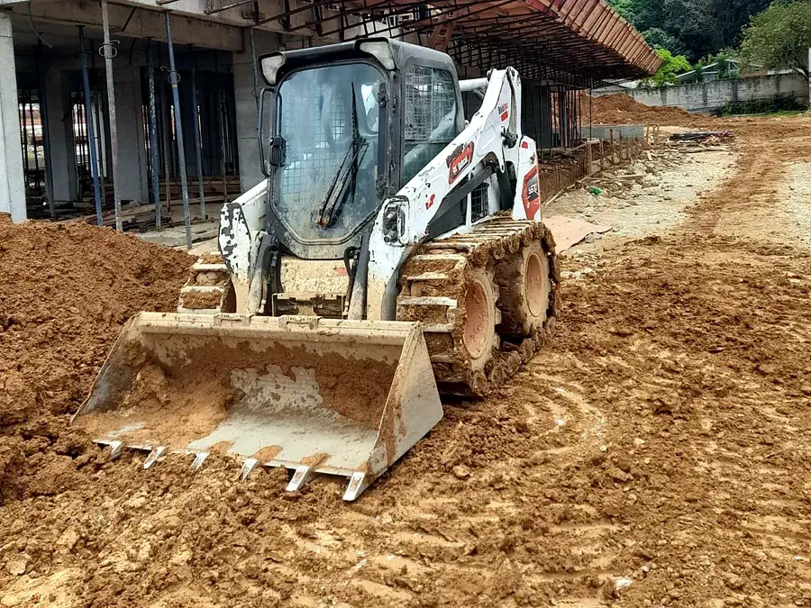Bobcat S570 com esteira de aço sobre os pneus, de frente, trabalhando em terreno de barro